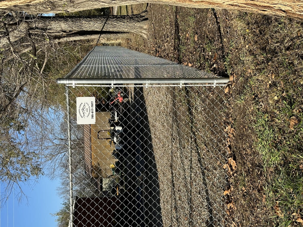 chain link fence with trees nearby and dirt on the floor